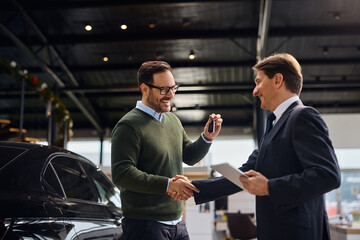 Happy man handshaking with salesman while holding key of his new car.