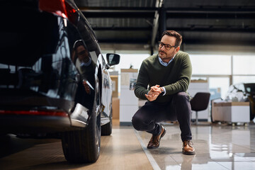Smiling man examining new car in a showroom.