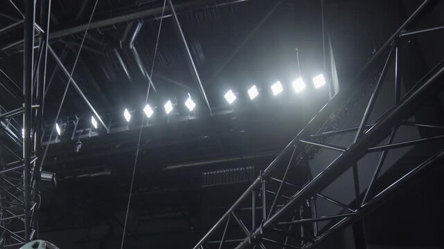 Metal beam carcass hangs under illuminated concert hall ceiling low angle shot. Light weight frames for equipment fastening over show stage