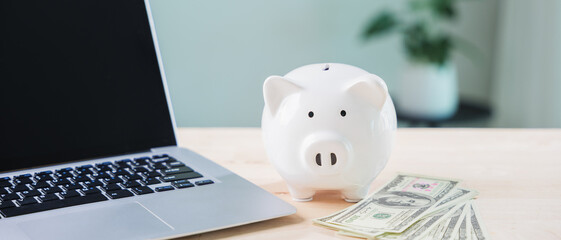 piggy bank online money elearning internet financial e learning education budget goals involve saving for courses beside laptop computer with cash on wooden surface in office