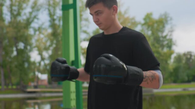 white man tattooed forearm adjusting boxing gloves in closeup, detailed leather straps and mitts, trainer or fighter tightening grip, raw texture and sweat, lakeside backdrop, intense preparation