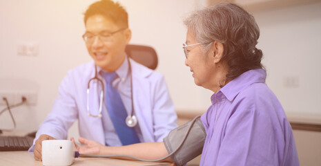 A male doctor is consulting with an elderly patient, discussing how to take the patient's temperature at the clinic.