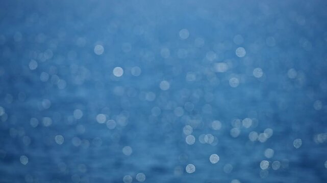 Blurry ocean texture glows. Light sparkles on blue water. Glowing sea feels peaceful. Bokeh dots float on ocean. Soft shine covers the sea. Blurry waves glow quietly. Ocean light flickers softly.