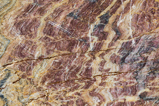 vista macro di una superficie lavorata e liscia di marmo rosso scuro naturale, ricco di sfumature di colore giallo sbiadito e grigio e venature bianche