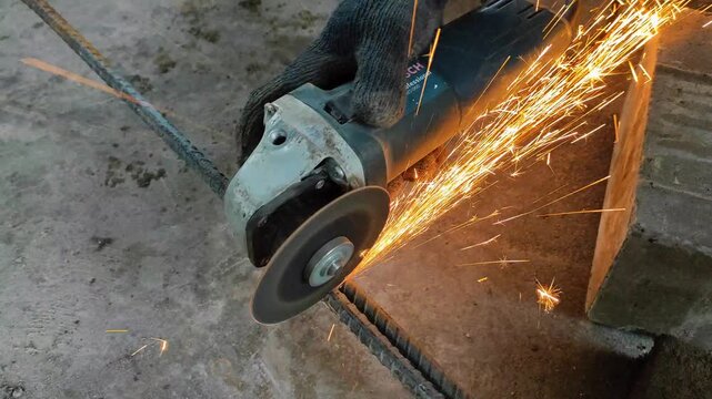 Close-up of cutting a steel rod with an angle grinder, sending bright sparks across a workshop floor. Shows metalworking, construction process, tools, and safety in industrial work.