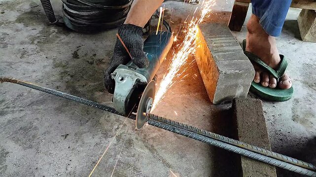 Dangerous work with an angle grinder, sparks flying everywhere as a worker cuts rebar wearing only flip-flops. 