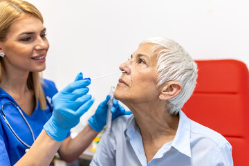 Medical professional in blue uniform performing a nasal swab test on a senior woman for virus detection or allergy screening during a medical examination in a bright clinical environment