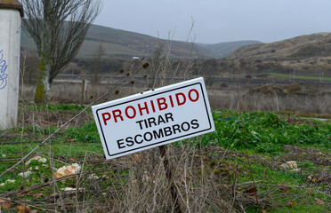 Tilted &ldquo;No dumping&rdquo; warning sign standing in an abandoned field under an overcast sky, symbolizing urban decay and the consequences of failed real estate development and land neglect.