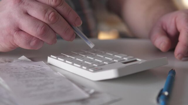 White Man Double Checking Totals With Pen And Calculator On Desk, Meticulous Hand Taps And Close Ledger Inspection, Professional Audit Vibe In Warm Interior Light, Compliance Focused
