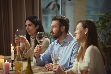 Friends in their thirties drinking wine at dinner table in cozy home interior. Concept of wine...