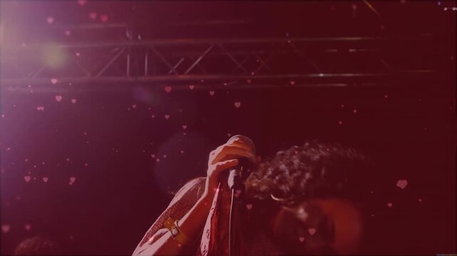 Singer singing into mic on red-pink stage with music building, fueling hair flicks, heart overlays