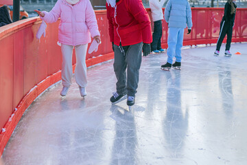 Obraz premium Two people at the edge of skating rink barrier. Man coach in red and woman in pink, beginner skater. Ice skating on ice rink arena with people. Concept of sport support, winter sport, health, hobby