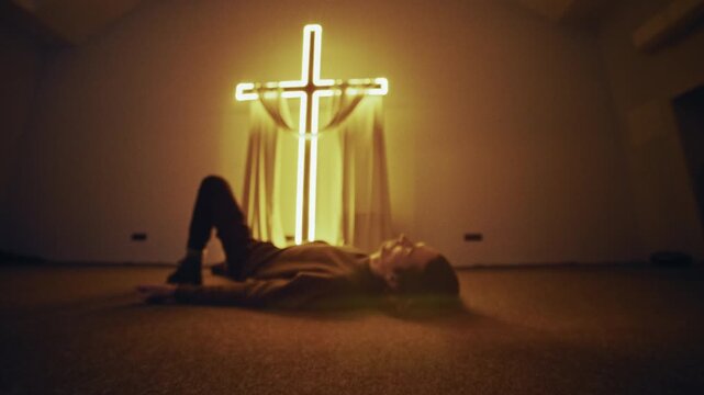 In a darkened space, a youthful believer is captured in a moment of deep, personal prayer while laying on the floor.