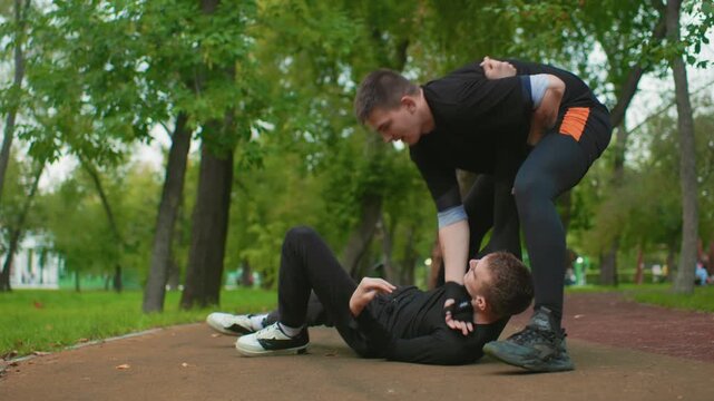 park grapple takedown scene showing two men sparring on treelined path, aggressive clinch, ground pin, defender escaping while attacker releases and walks away, raw urban training vibe with heavy
