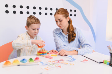 Boy learning fine motor skills with tutor in classroom