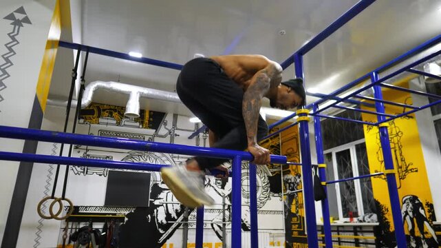 Muscular african sportsman trying to do handstand on parallel bars at sport club. Young afro american athlete practicing stunts on uneven bars at modern gym. Strong black man training indoor