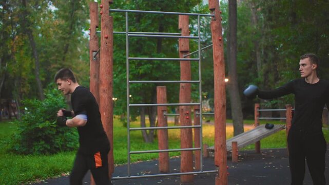 caucasian men sparring with focus pad in sunset park, trainee launches high kick while trainer holds mitt, energetic motion and impact, teamwork driven training, athletic demonstration and skillful