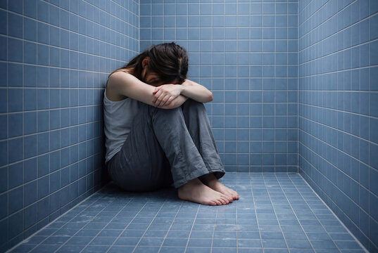 Depressed woman sitting alone in tiled room corner