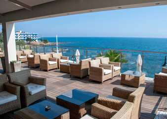 Fototapeta premium Elegant Ocean View Terrace With Wicker Lounge Chairs And Glass Railings At Seaside Resort