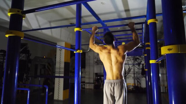 Muscular sportsman doing pull ups on horizontal bar at modern gym. Strong male athlete working out at sport club. Young sportsperson exercising at fitness centre. Concept of healthy active lifestyle