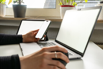 Modern workspace showing multitasking with laptop and and phone, hand on an ergonomic mouse, clean mockup screens, cozy home office, natural daylight, minimal desk and potted plants.