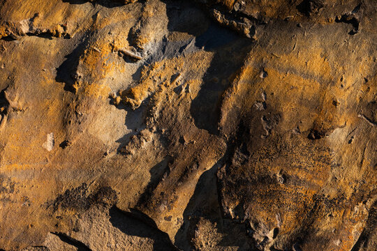 vista macro di una superficie rocciosa ruvida e naturale, dalle sfumature di colore marrone, illuminata dal sole, con vari effetti di ombre e rilievi casuali sulla superficie