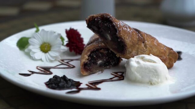 Close-up of a beautifully plated dessert. A freshly baked strudel with a fruity filling, served with a scoop of vanilla ice cream and jam