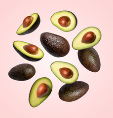 Avocados whole and halved falling on pink background