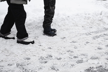 Adult and child standing on icy snow-covered sidewalk with visible footprints and slush, highlighting hazardous walking conditions due to inadequate municipal snow removal after winter storm