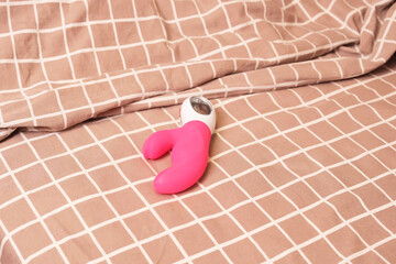 Close-up of vibrant pink sex toy lying on textured checkered duvet near folded fabric, capturing...