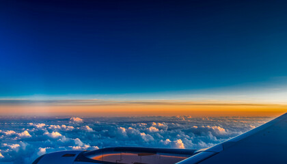 Aerial view of airplane wing flying above clouds with dramatic deep blue sky and orange sunset horizon