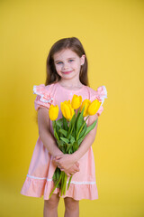 Cheerful happy girl with tulips flower bouquet in pink dress on yellow background