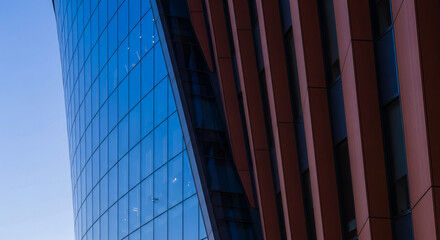 Exterior close-up of a modern building with blue glass facade and parallel architectural structure. Representative of urban development, design, or finance