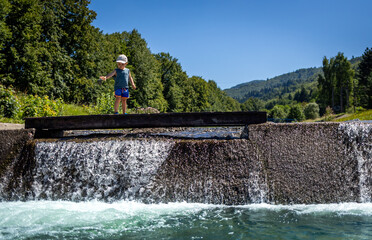 Child walks near a waterfall on a mountain stream, vacation time in the mountains during the summer