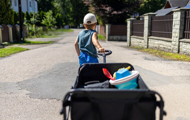 Child pulls a four-wheel folding wagon with toys and accessories during a tourist trip