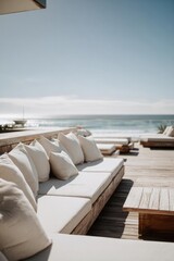 Fototapeta premium Sunlit beachside deck with cream cushions and wooden tables, overlooking the calm ocean. Concept Beachside deck, Sunlit atmosphere, Cream cushions, Wooden tables, Calm ocean view