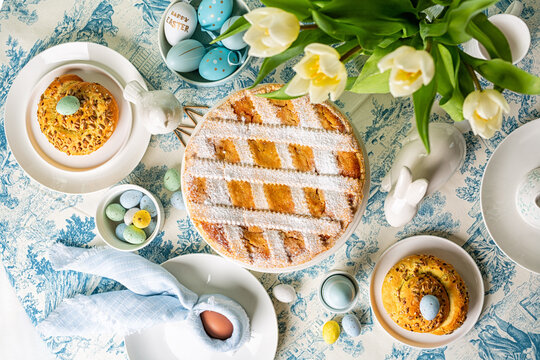 Served Easter round dining table directly above, Italian Easter cake, shortcrust pie with ricotta cheese, Pastiera Napoletana, colorful eggs, buns, easter bunny and bird sculptures,  tulips flowers. 