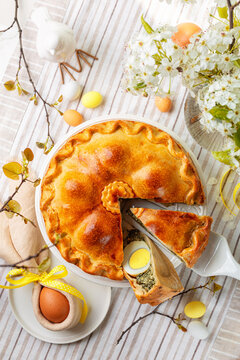 The Torta Pasqualina, a savory Easter pie made with spinach, silverbeet, cheese and eggs, originated in Italy, Liguria.  Homemade bakery. Festive Easter table, with colored eggs, flowers. Vertical.