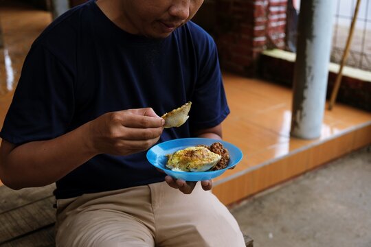 Man eating traditional Indonesian serabi snack on a plate, representing local cuisine, casual dining, cultural food habits, and authentic everyday lifestyle indoors.