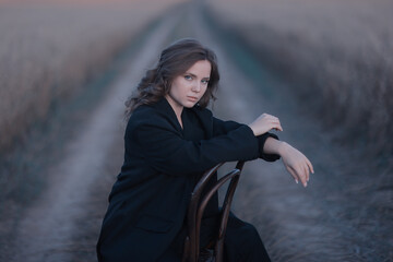 A female model poses sitting on a chair among nature and fields, an unusual photo of a summer Look