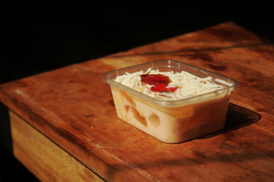 Healthy food for breakfast, a simple fruit salad with lots of cheese toppings and strawberry slices in a plastic box on an aesthetic table bathed in morning sun.