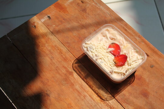 Healthy food for breakfast, a simple fruit salad with lots of cheese toppings and strawberry slices in a plastic box on an aesthetic table bathed in morning sun.