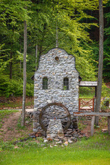 A decorative stone structure features an old wooden water wheel set against a lush green forest background.