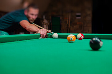 A focused man in a dimly lit pool hall leans over a green felt table to take a precise shot with his cue stick.