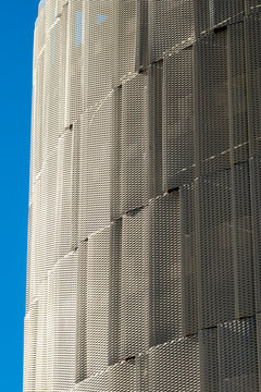 Modern urban architecture facade with perforated metal texture and repeating pattern under blue sky creating abstract copy space background