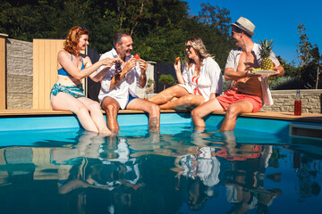 Group of middle aged friends enjoying fruit and drinks by swimming pool.