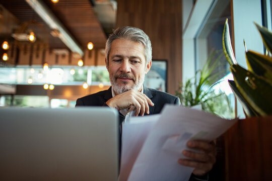 Mature businessman reviewing documents on laptop in cafe