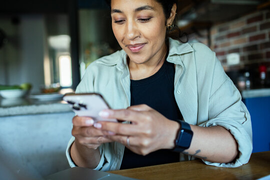 Smiling woman using smartphone at kitchen table