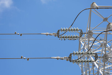 Low angle close-up of electrical transmission tower's insulators, fittings, and other components connecting high-voltage power lines to the large metal lattice tower.