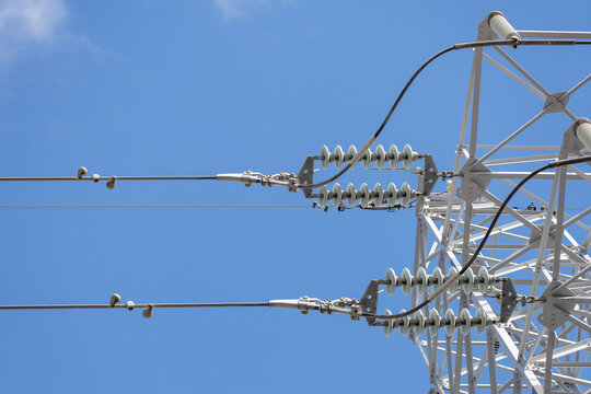 Low angle close-up of electrical transmission tower's insulators, fittings, and other components connecting high-voltage power lines to the large metal lattice tower.